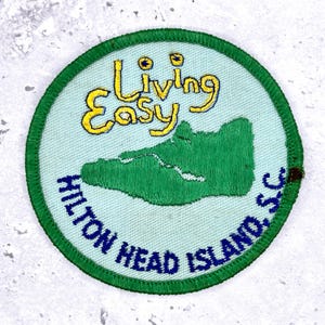 May include: Circular patch with a green border and a light blue center. The patch features the text "Living Easy" in yellow script above a green island graphic. The words "HILTON HEAD ISLAND, SC" are in blue, encircling the bottom.