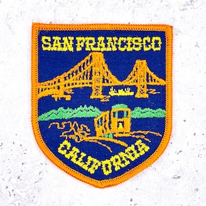 May include: A blue and orange patch featuring the words "SAN FRANCISCO CALIFORNIA". The patch depicts the Golden Gate Bridge, a cable car, and green hills. The patch has an orange border.