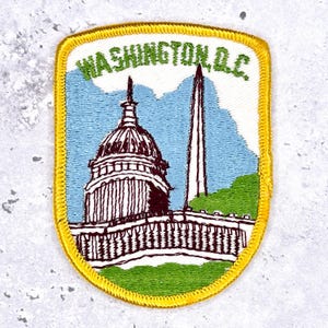 Può includere: Toppa ricamata con monumenti di Washington, D.C. Il design include il Campidoglio e il Monumento a Washington, su uno sfondo di cielo blu e paesaggio verde. La toppa ha un bordo giallo e la scritta "WASHINGTON, D.C."