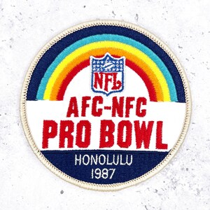 May include: Circular patch with a rainbow design and the NFL logo. The text "AFC-NFC PRO BOWL HONOLULU 1987" is displayed in red and white on a navy blue background. The patch has a cream-colored border.