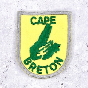 May include: A yellow patch featuring a green map of Cape Breton Island, with the words "CAPE BRETON" in green. The patch is edged with a grey border.