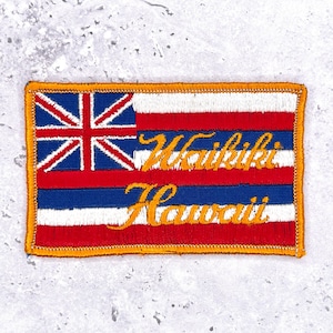 May include: Embroidered patch featuring the Hawaiian flag design with the Union Jack in the upper left corner. The patch includes the words "Waikiki Hawaii" in a gold script font, outlined in orange.