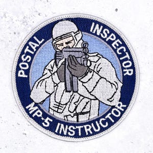 May include: A circular embroidered patch featuring a figure in a white tactical uniform and helmet holding a black submachine gun. The background is light blue, surrounded by a dark blue border with the text POSTAL INSPECTOR MP-5 INSTRUCTOR.