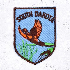 Może przedstawiać: Zestaw trzech ceramicznych kubków z nakrapianym, matowym wykończeniem. Kubki są w odcieniach kremu, jasnoszarym i ciemnoszarym. Każdy kubek ma prosty, nowoczesny design i zaokrąglony uchwyt. Kubki są ułożone jeden na drugim.