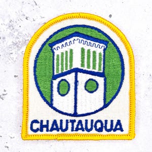 May include: An embroidered patch with a yellow border, featuring a white building with green accents inside a green circle outlined in blue. The building has a crenelated top and two circular windows. The word CHAUTAUQUA is stitched in blue at the bottom.