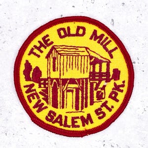 Peut inclure: Un écusson circulaire avec un centre jaune et une bordure rouge. L'écusson présente une illustration marron d'un moulin et le texte "THE OLD MILL NEW SALEM ST. PK."
