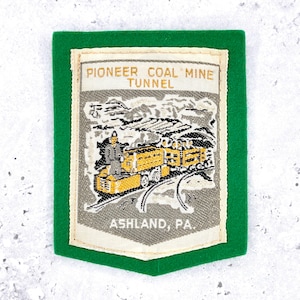 May include: A rectangular patch with a green border and a central image depicting a coal mine tunnel. The text "PIONEER COAL MINE TUNNEL" is at the top, with "ASHLAND, PA" at the bottom. The image shows a yellow train on tracks.