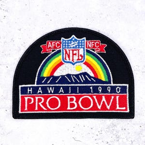 Op de afbeelding: Zwarte patch met het NFL-logo, een regenboog en de tekst "HAWAII 1990 PRO BOWL". De patch heeft rode, blauwe, gele en groene accenten. De AFC- en NFC-logo's zijn ook zichtbaar.
