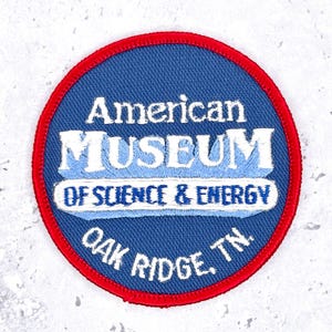 Peut inclure: Un écusson brodé circulaire avec un fond bleu et une bordure rouge. Le texte indique American MUSEUM OF SCIENCE & ENERGY OAK RIDGE, TN. en lettres blanches et bleu clair. L'écusson présente un design aux bords cousus nets.
