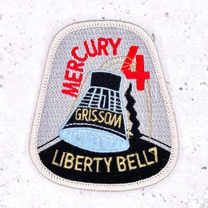 Puede incluir: Parche bordado que representa la misión Mercury 4 Liberty Bell 7. El parche tiene un fondo gris con texto "MERCURY" en rojo, un número "4" rojo y un diseño de cápsula negro y azul con texto "GRISSOM" y "LIBERTY BELL 7".