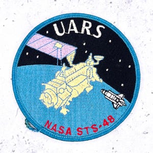 May include: Embroidered patch featuring a space-themed design. The patch has a blue border and depicts a spacecraft, a shuttle, and the text "UARS" and "NASA STS-48". The background includes a starry night sky and a light blue planet surface.