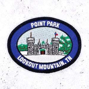 Könnte beinhalten: Ein ovaler gestickter Aufnäher mit blauem Rand und dem weißen Text POINT PARK sowie LOOKOUT MOUNTAIN, TN. Die Mitte zeigt ein weißes steinernes Burgtor mit zwei Türmen, grünen Bäumen und einer kleinen rot-blauen Flagge an einem Mast.