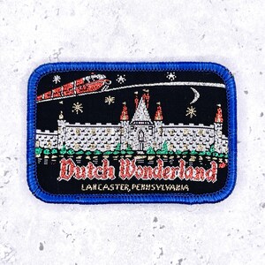 May include: A rectangular embroidered patch with a blue border featuring a black background, a white castle with red turrets, a red monorail, stars, and a crescent moon. The text reads Dutch Wonderland and Lancaster, Pennsylvania in red and white.