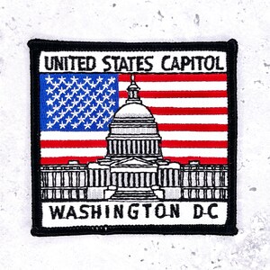 May include: Embroidered patch featuring the United States Capitol building with the American flag. The patch has a black border and includes the text "UNITED STATES CAPITOL" and "WASHINGTON D.C."