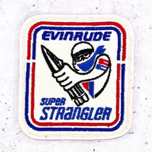 May include: A square embroidered patch with rounded corners featuring a white background, a red and blue border, and the text "EVINRUDE" and "SUPER STRANGLER" in blue. A graphic depicts a stylized figure holding a pointed tool in blue and black.
