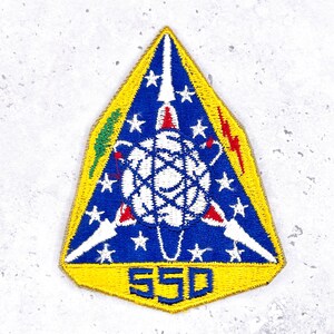 May include: Embroidered patch in a triangular shape with a yellow border. The patch features a blue background with white stars, a white and red central design, and the number "550" in yellow. Additional details include lightning bolts and a green element.