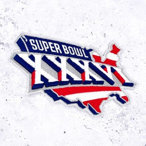 Könnte beinhalten: Gestickter Aufnäher in Form der Vereinigten Staaten, mit dem Text "SUPER BOWL LVII" in Weiß auf blauem Hintergrund. Der Aufnäher hat rot-weiße Streifen und einen silbernen Rand.