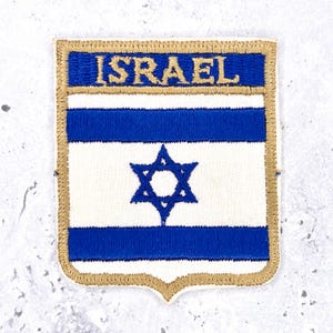 May include: Embroidered patch of the Israeli flag. The design features a blue Star of David on a white background, with blue stripes above. The word "ISRAEL" is embroidered in gold thread at the top, with a gold border.