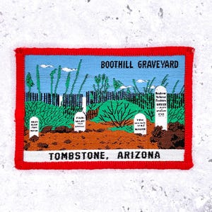 Può includere: Una toppa rettangolare con bordo rosso raffigura il cimitero di Boothill a Tombstone, in Arizona. L'immagine include lapidi, fogliame verde e il testo "Boothill Graveyard" e "Tombstone, Arizona."