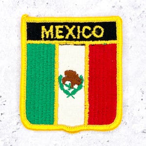 May include: Embroidered patch featuring the Mexican flag. The rectangular patch has a black top border with the word "MEXICO" in yellow. The flag design includes green, white, and red vertical stripes, with the Mexican coat of arms in the center.