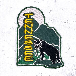 May include: Embroidered patch featuring a black bear silhouette on a green mountain landscape. The word "Tennessee" is vertically stitched in yellow. The patch has a white border and a light gray background.