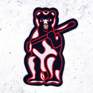 May include: An embroidered patch featuring a black bear standing upright and holding a baseball bat across its chest. The bear design is outlined in vibrant red thread, with white accents on its chest, legs, and the bat, creating a bold contrast.