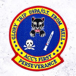May include: Embroidered patch with a blue center featuring a black panther, skull and crossbones, and a white object. The patch has yellow and red borders with text that reads "GLORY TRIP 09PA/O.T. FROM HELL" and "ACC'S FIRST PERSEVERANCE".