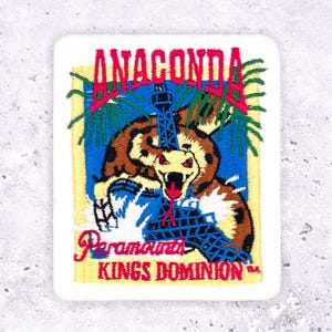 May include: Embroidered patch featuring the word "ANACONDA" in pink and a cartoon snake with an open mouth. The patch also includes the text "Paramount's KINGS DOMINION" in red, with a blue and yellow background.