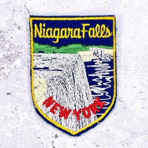 May include: Embroidered patch featuring Niagara Falls, with the text "Niagara Falls" in yellow and "NEW YORK" in red. The patch has a blue background with a yellow border, depicting the waterfall and surrounding landscape.