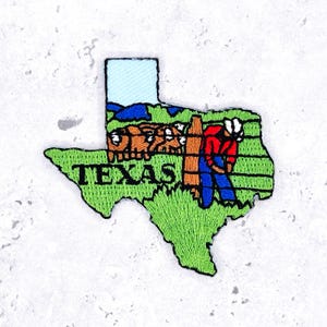 May include: Embroidered patch in the shape of Texas, featuring a green outline with the word "TEXAS" in green. The patch depicts a cowboy, cattle, and a blue sky. The patch is approximately 2.5 inches wide and 2 inches tall.