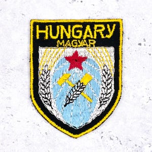 May include: Embroidered patch featuring the word "HUNGARY" above "MAGYAR" in yellow text on a black background. The patch has a shield design with a red star, yellow hammer and wheat, and a light blue background. The border is black and yellow.