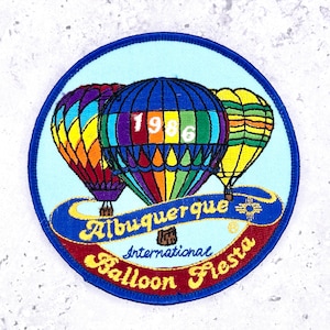 May include: Embroidered patch featuring three colorful hot air balloons against a light blue background. The patch reads "Albuquerque International Balloon Fiesta" with the year "1986" on the central balloon. The patch has a blue border.