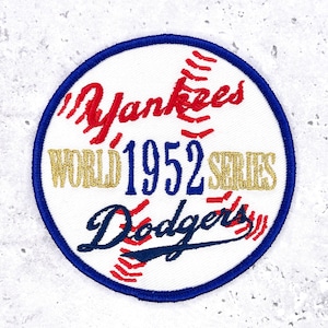 May include: Embroidered patch featuring a baseball design with the text "Yankees WORLD 1952 SERIES Dodgers." The patch has a white background, red stitching, blue border, and gold lettering. A vintage sports collectible.