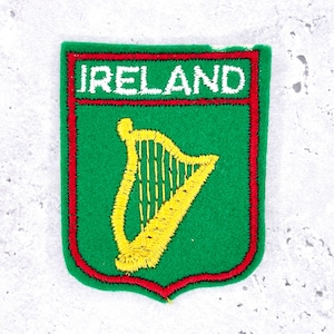 May include: A green patch with a red border and the word "IRELAND" in white. The patch features a yellow harp, a symbol of Ireland. The patch is likely an emblem or souvenir.