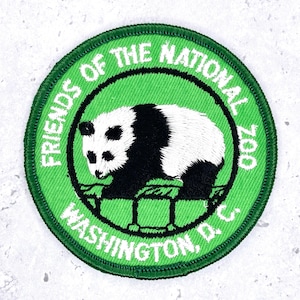 May include: A circular embroidered patch with a bright green background and a dark green border. The center features a black and white panda standing on a stylized green structure. The text reads FRIENDS OF THE NATIONAL ZOO WASHINGTON, D.C.