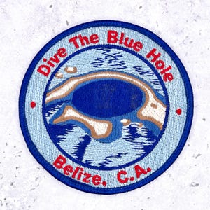 May include: A circular embroidered patch featuring a depiction of the Blue Hole in Belize. The design includes a dark blue center surrounded by light blue water and tan land, with the red text Dive The Blue Hole and Belize, C.A. stitched along the border.
