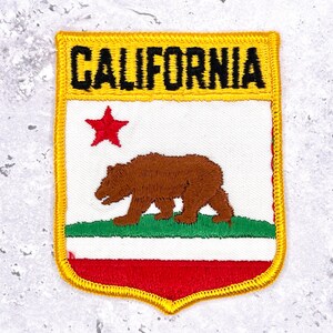 Peut inclure: Écusson brodé représentant le drapeau de l'État de Californie. Le patch a une bordure jaune et le mot "CALIFORNIA" en noir. Le motif comprend un ours brun, une étoile rouge et les couleurs de l'État : rouge, blanc et vert.