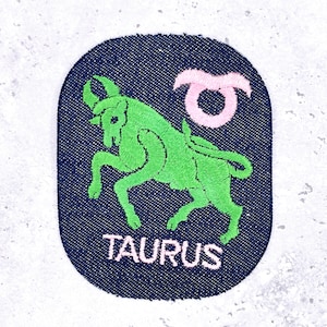 May include: Embroidered patch featuring the Taurus zodiac sign. The design includes a green bull and a pink Taurus symbol on a navy blue background. The word "TAURUS" is embroidered in pink below the image.