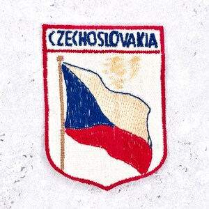 May include: Embroidered patch featuring the flag of Czechoslovakia. The flag is depicted in red, white, and blue, with the word "CZECHOSLOVAKIA" embroidered in blue at the top. The patch has a red border.