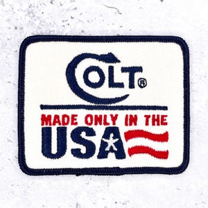 May include: A rectangular embroidered patch with a white background and a dark blue border. It features the dark blue Colt logo, followed by the red text MADE ONLY IN THE USA, with the letters USA in dark blue, a white star, and red stripes.