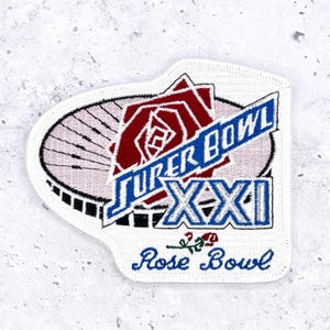 May include: An embroidered patch featuring a stylized stadium graphic with a red rose icon. The text reads SUPER BOWL XXI in blue and white, with the words Rose Bowl in blue script below, accompanied by a small embroidered red rose and green stem.