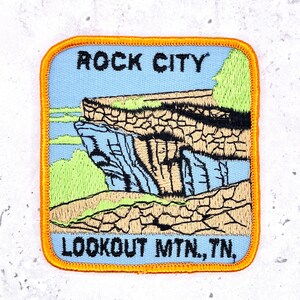 May include: Square patch with an orange border featuring the text "ROCK CITY" and "LOOKOUT MTN., TN." The patch depicts a scenic view of a rock formation with a blue sky background, green foliage, and tan rock details.