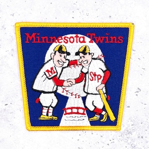 May include: A square patch with a blue background and a yellow border. The patch features the words "Minnesota Twins" in red. Two cartoon baseball players shake hands in front of a baseball. The player on the left has an "M" on his shirt, and the player on the right has "Stp".