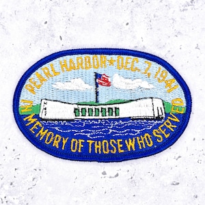 May include: An oval patch with a blue border and the text "PEARL HARBOR * DEC. 7, 1941" and "IN MEMORY OF THOSE WHO SERVED" in gold lettering. The patch features a depiction of a structure, an American flag, and water.