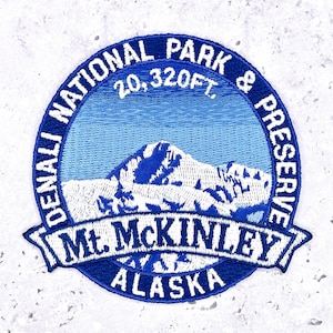 May include: Embroidered patch featuring a mountain landscape with the text "DENALI NATIONAL PARK & PRESERVE" and "Mt. McKinley ALASKA". The patch is circular with a blue and white color scheme, and the mountain is depicted in shades of blue.