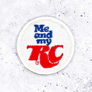 May include: Round, white embroidered patch with the text "Me and my RC" in blue and red. The patch has a stitched border and is likely for clothing or accessories.