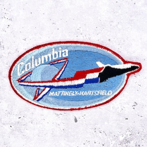 May include: Embroidered patch featuring a stylized airplane design in red, white, blue, and black. The patch has the word "Columbia" arched across the top and "MATTINGLY-HARTSFIELD" at the bottom, set against a light blue background.