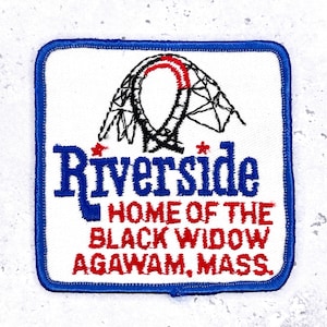 May include: Square patch with a blue border and white background. The patch features the word "Riverside" in blue, a roller coaster graphic, and the text "HOME OF THE BLACK WIDOW AGAWAM, MASS." in red.