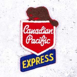 Może przedstawiać: Haftowana naszywka z brązowym bobrem nad czerwoną tarczą z białym napisem "Canadian Pacific". Poniżej, niebieski prostokąt z napisem "EXPRESS" w kolorze żółtym.