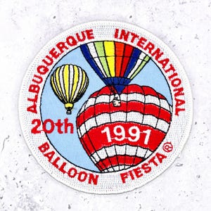 May include: Embroidered patch featuring the Albuquerque International Balloon Fiesta. The design includes two hot air balloons, one yellow and one red and white striped, with the text "Albuquerque International Balloon Fiesta 20th 1997".